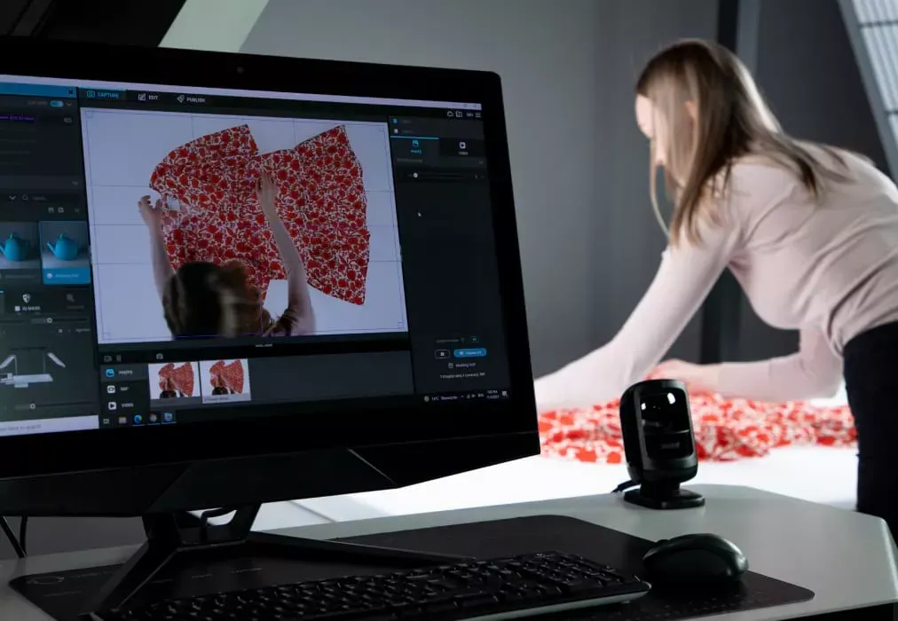 Fotograf richtet ein Kleidungsstück mit floralem Stoff aus, während die Live-Ansicht auf dem Monitor zu sehen ist