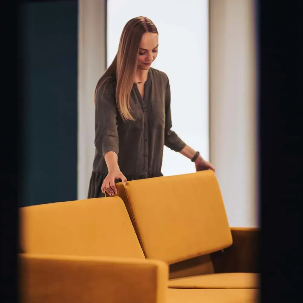 Frau arrangiert Kissen auf einem gelben Sofa für ein Fotoshooting